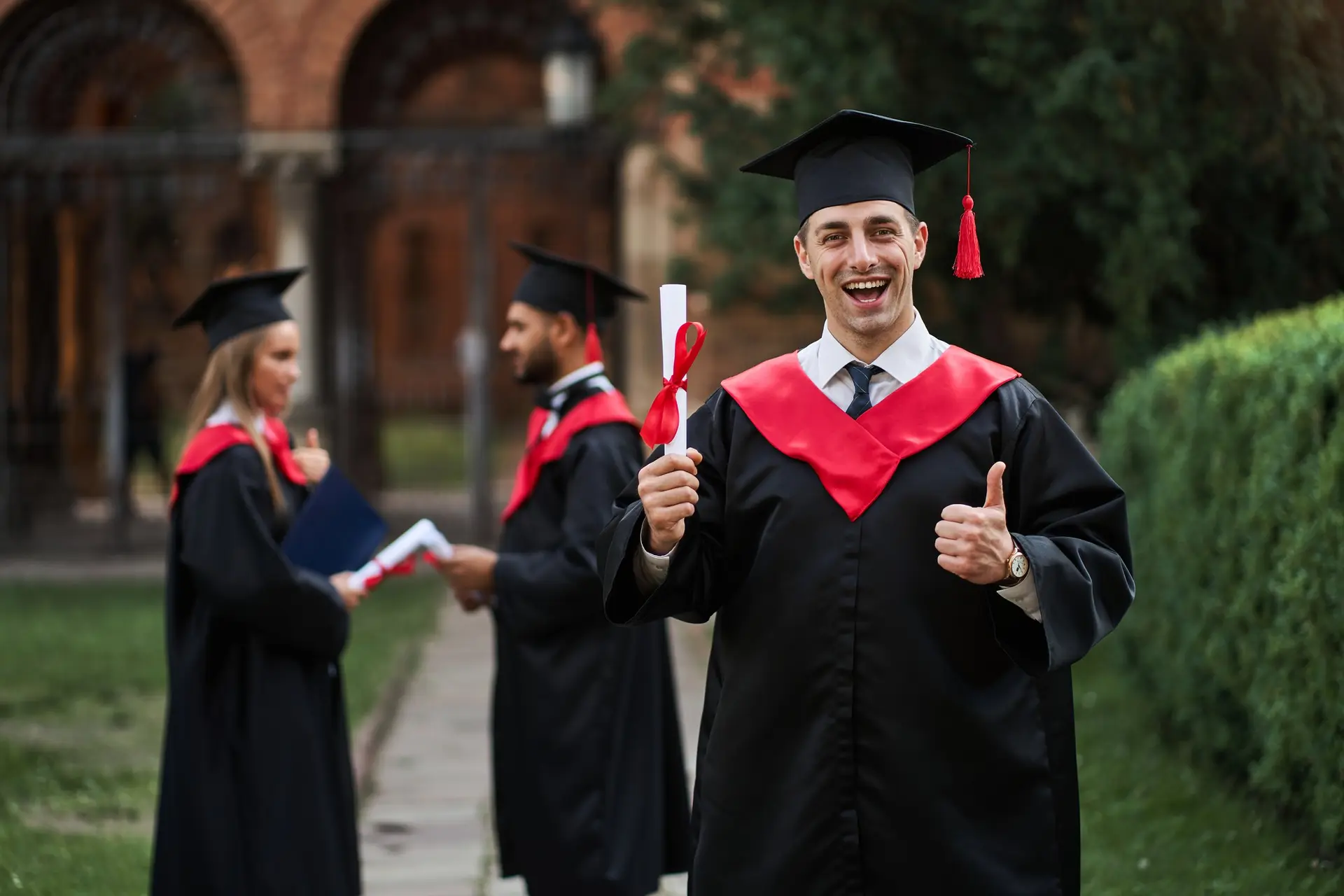 Three graduates in gowns and caps celebrating outside a university building