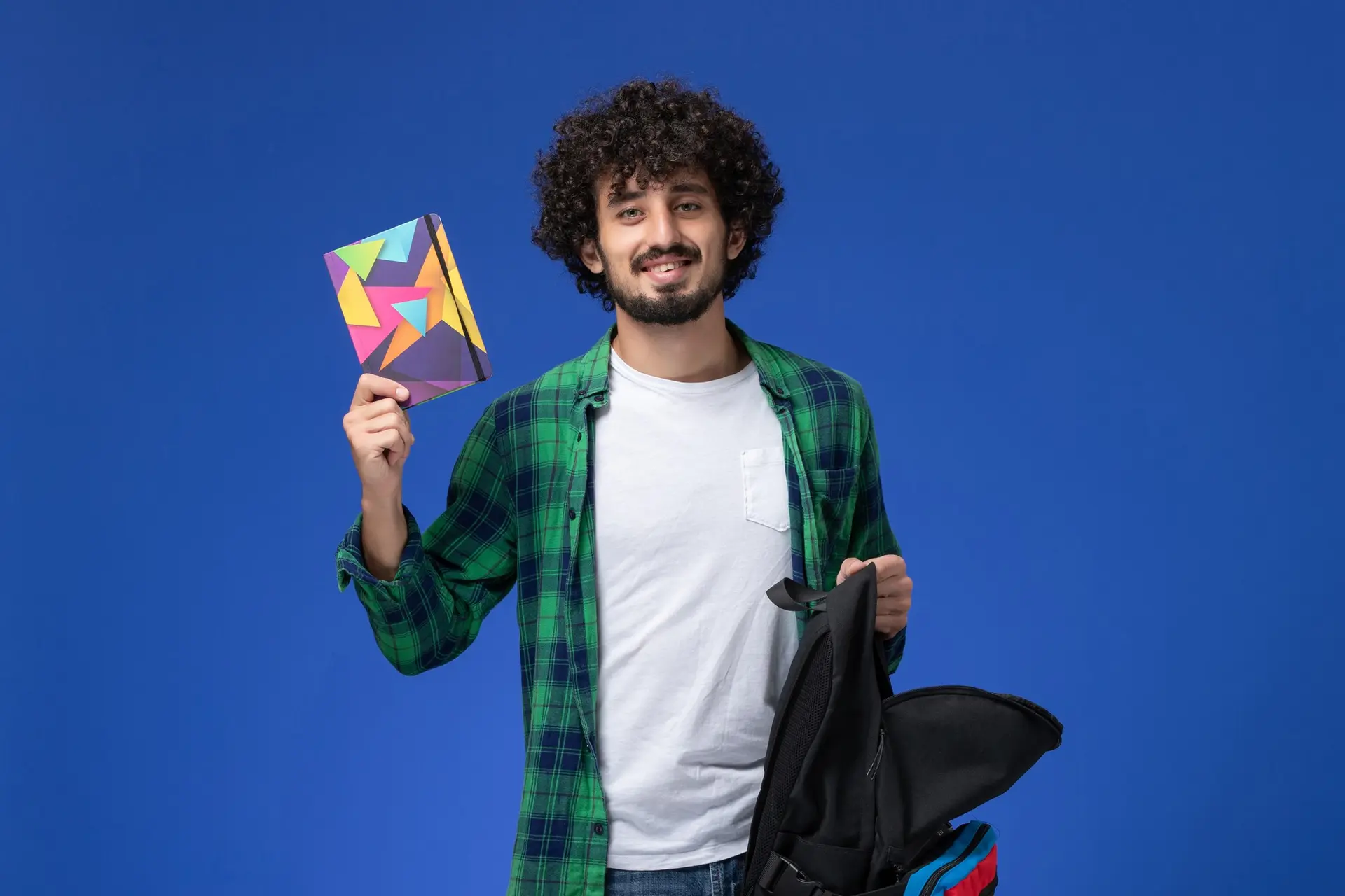 A student with a backpack holding up a notebook against a blue background