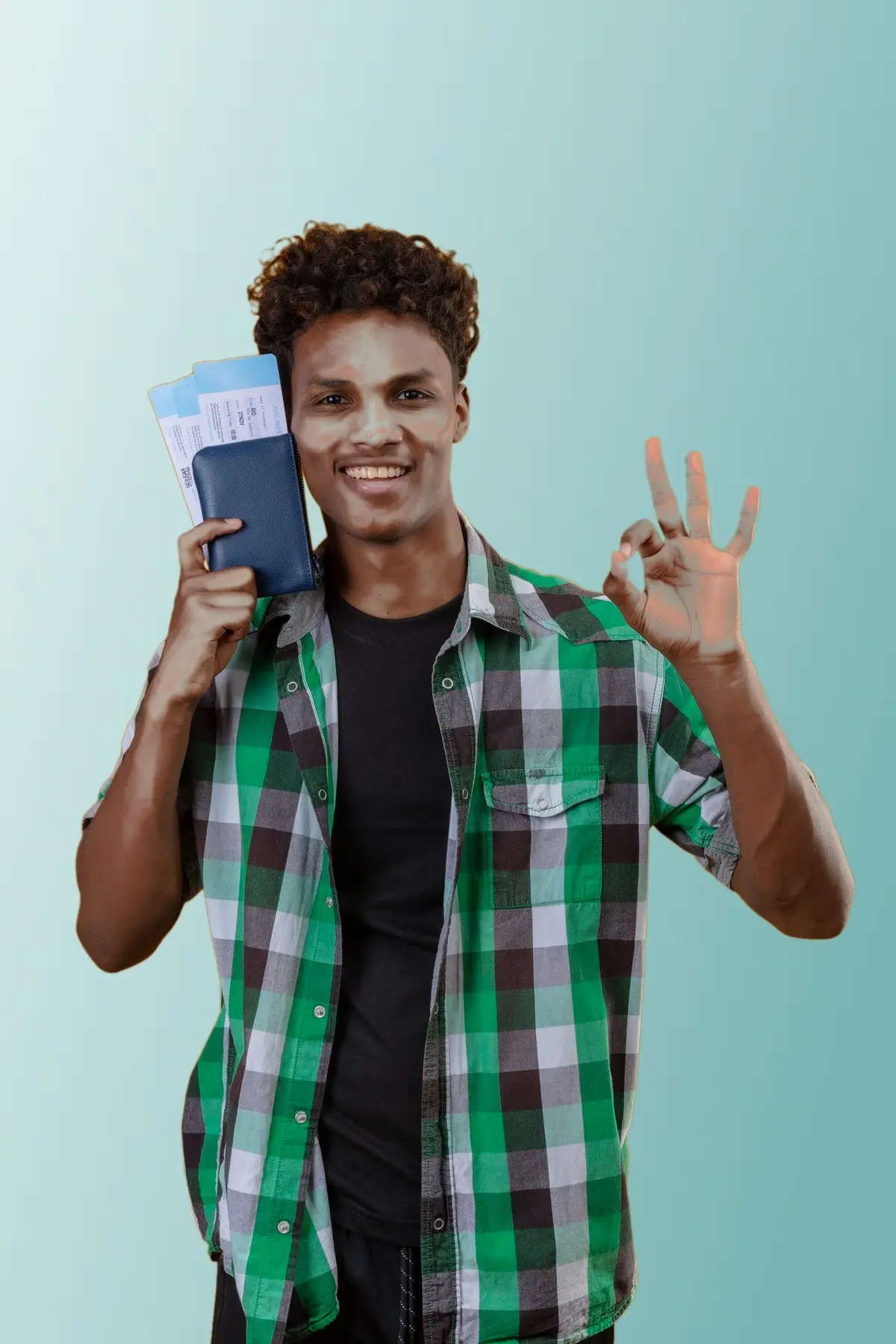 A smiling student holding a passport and boarding passes, making an OK sign